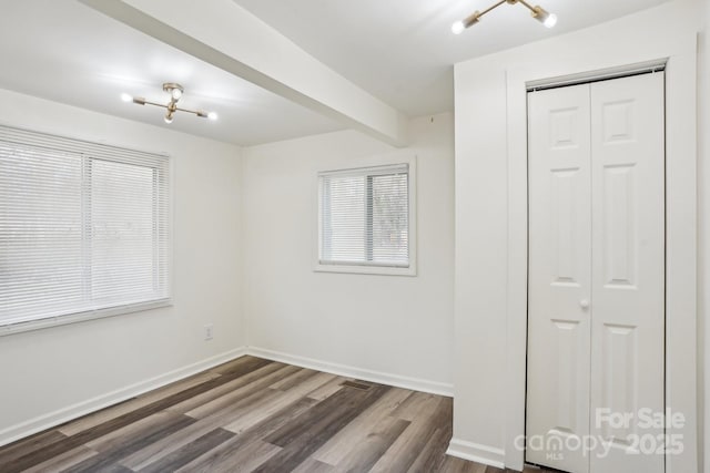 spare room with beamed ceiling and dark wood-type flooring