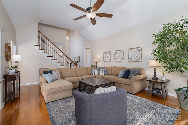 living area featuring baseboards, stairway, vaulted ceiling, wood finished floors, and a ceiling fan