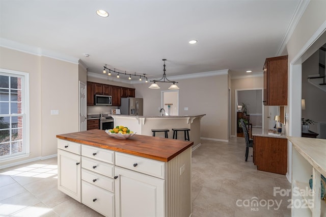 kitchen with wooden counters, a kitchen island, recessed lighting, ornamental molding, and appliances with stainless steel finishes