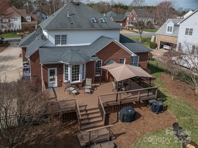 back of property featuring fence, roof with shingles, a wooden deck, outdoor dining area, and brick siding