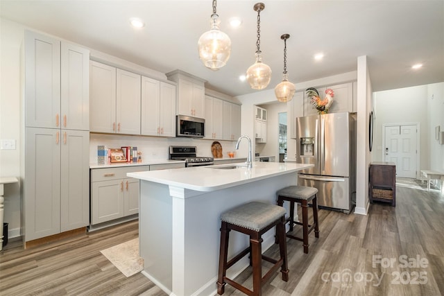 kitchen featuring decorative light fixtures, stainless steel appliances, light hardwood / wood-style floors, and a center island with sink