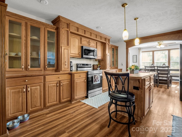 kitchen with a kitchen island, appliances with stainless steel finishes, backsplash, hardwood / wood-style flooring, and hanging light fixtures