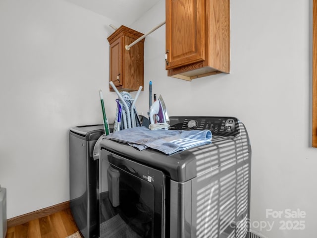 clothes washing area featuring washer and dryer, hardwood / wood-style flooring, and cabinets