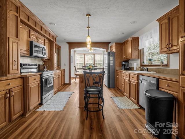 kitchen with sink, a breakfast bar, appliances with stainless steel finishes, decorative light fixtures, and light wood-type flooring