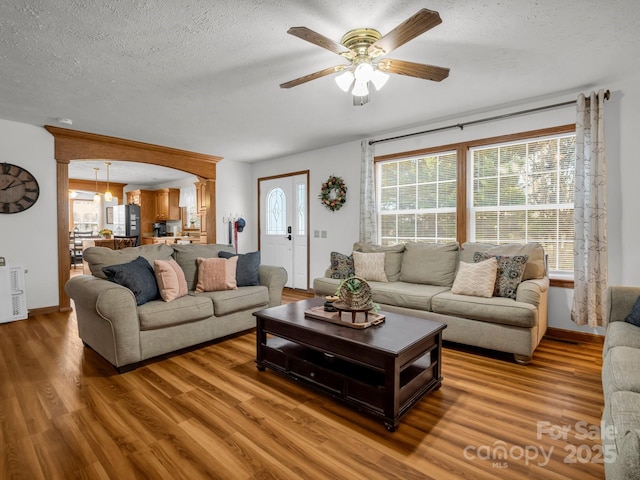 living room featuring hardwood / wood-style flooring, ceiling fan with notable chandelier, and a textured ceiling