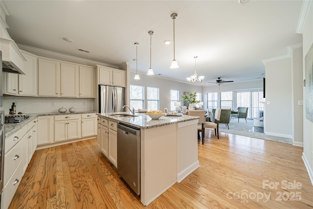 kitchen with appliances with stainless steel finishes, decorative light fixtures, an island with sink, ornamental molding, and light stone countertops