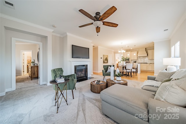 living room with light carpet, ceiling fan with notable chandelier, and ornamental molding