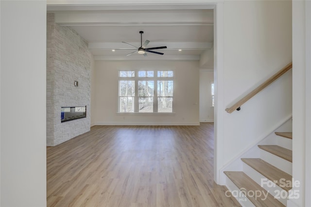 unfurnished living room featuring beamed ceiling, ceiling fan, a fireplace, and light hardwood / wood-style floors