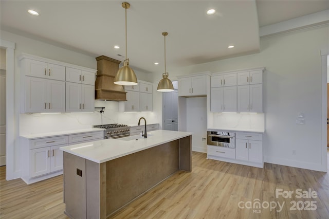 kitchen with pendant lighting, an island with sink, custom range hood, and white cabinets