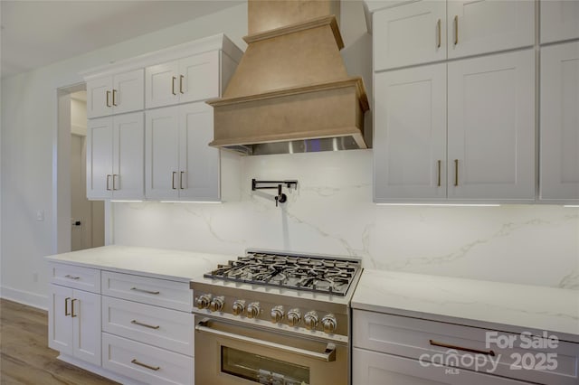 kitchen with premium range hood, high end stove, tasteful backsplash, white cabinets, and light stone counters