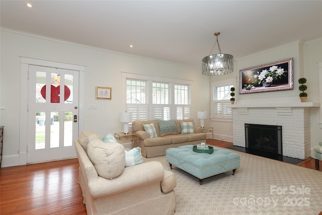 living room with hardwood / wood-style floors, ornamental molding, a chandelier, and a brick fireplace