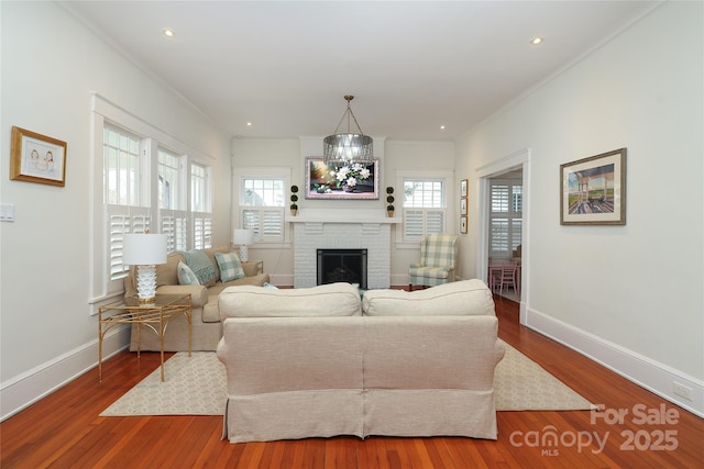 living room with an inviting chandelier, hardwood / wood-style floors, crown molding, and a fireplace