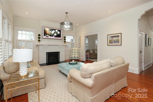 living room with ornamental molding, wood-type flooring, a fireplace, and a chandelier