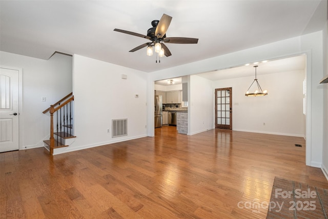 unfurnished living room featuring stairs, visible vents, light wood-style floors, baseboards, and ceiling fan with notable chandelier