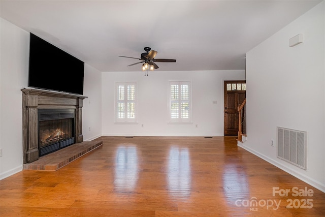 unfurnished living room featuring ceiling fan, a fireplace, visible vents, and wood finished floors