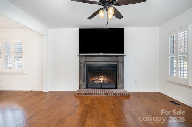 unfurnished living room featuring a warm lit fireplace, visible vents, baseboards, and wood finished floors