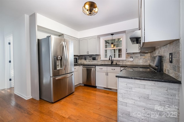 kitchen featuring tasteful backsplash, dark countertops, appliances with stainless steel finishes, light wood-style floors, and a sink