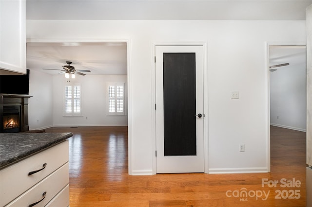 interior space with ceiling fan, white cabinetry, baseboards, light wood-style floors, and a glass covered fireplace