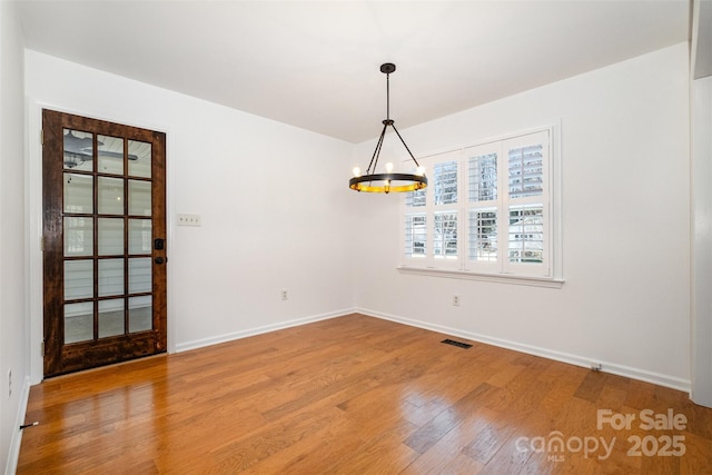 unfurnished dining area featuring an inviting chandelier, visible vents, baseboards, and wood finished floors