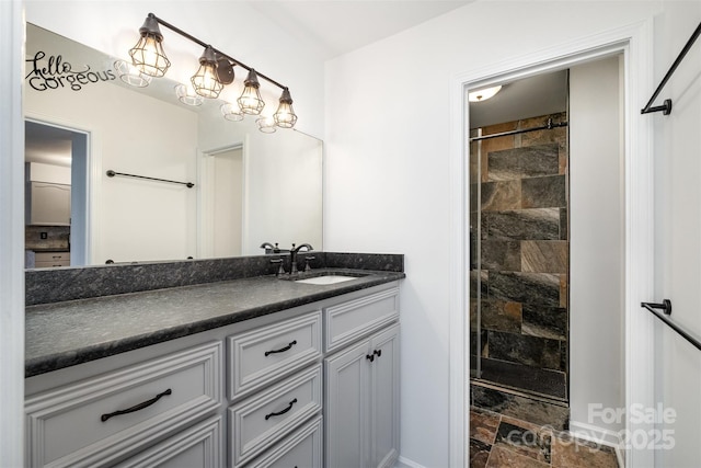 bathroom with stone finish flooring, baseboards, tiled shower, and vanity