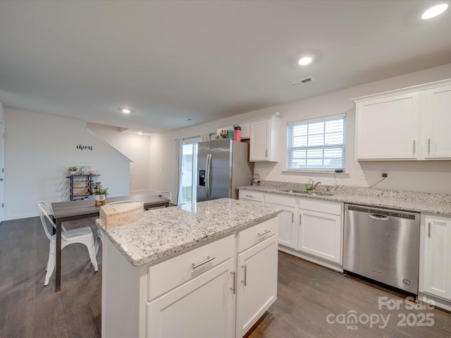 kitchen with white cabinetry, light stone counters, a center island, and appliances with stainless steel finishes