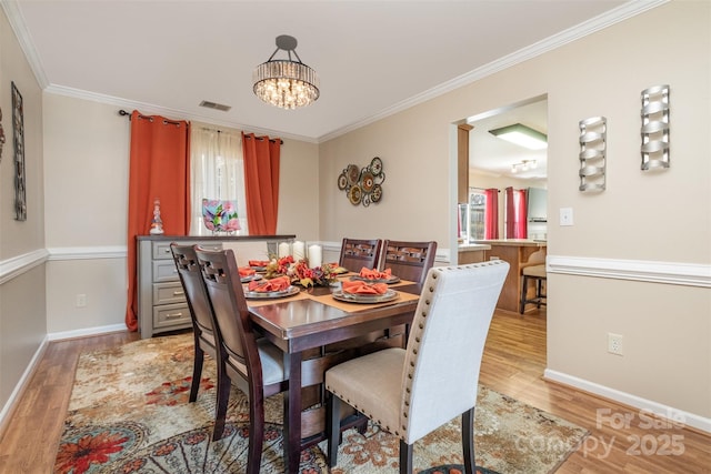 dining space with crown molding, a chandelier, and light hardwood / wood-style floors