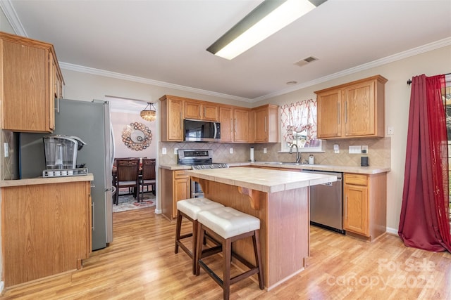 kitchen with sink, stainless steel appliances, a center island, a kitchen bar, and light wood-type flooring