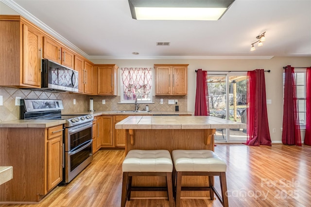 kitchen with sink, light hardwood / wood-style flooring, a center island, a kitchen bar, and range with two ovens