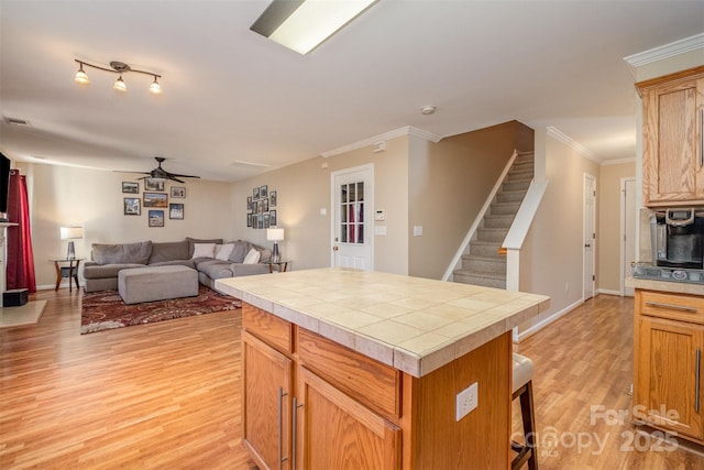 kitchen with a kitchen island, a breakfast bar area, ceiling fan, crown molding, and light wood-type flooring