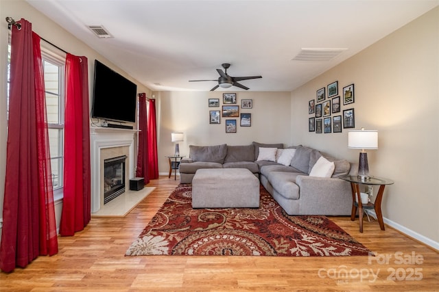 living room featuring ceiling fan, a high end fireplace, and light wood-type flooring