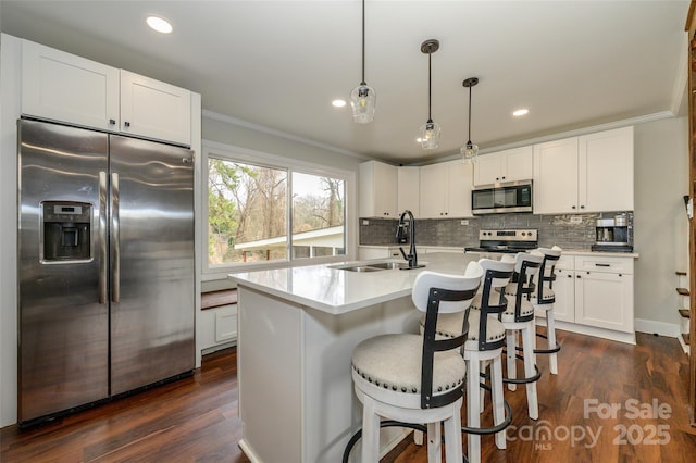 kitchen featuring appliances with stainless steel finishes, pendant lighting, white cabinetry, an island with sink, and sink