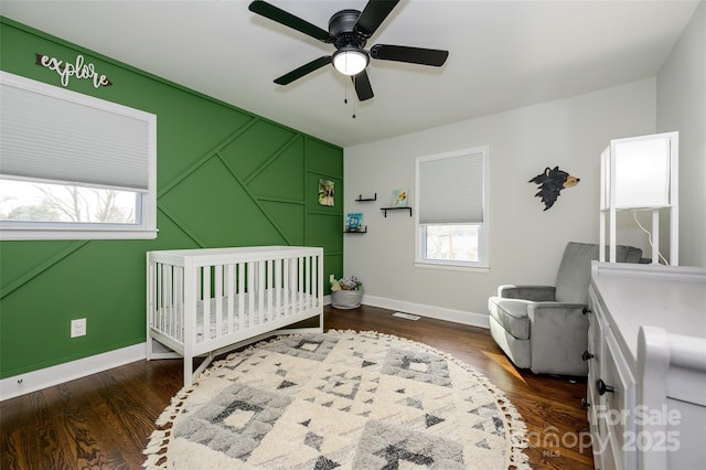 bedroom with dark hardwood / wood-style flooring, a crib, and ceiling fan