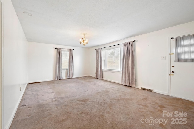 carpeted empty room with an inviting chandelier