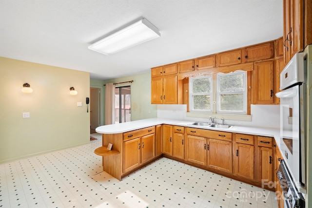 kitchen featuring a healthy amount of sunlight, kitchen peninsula, sink, and white oven