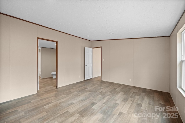 unfurnished room with ornamental molding, a textured ceiling, and light hardwood / wood-style floors