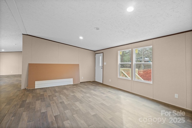 empty room with ornamental molding, a textured ceiling, and light wood-type flooring