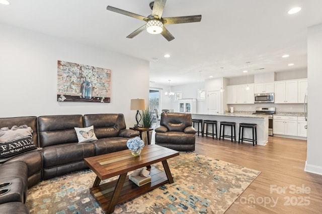 living room featuring ceiling fan with notable chandelier and light hardwood / wood-style floors