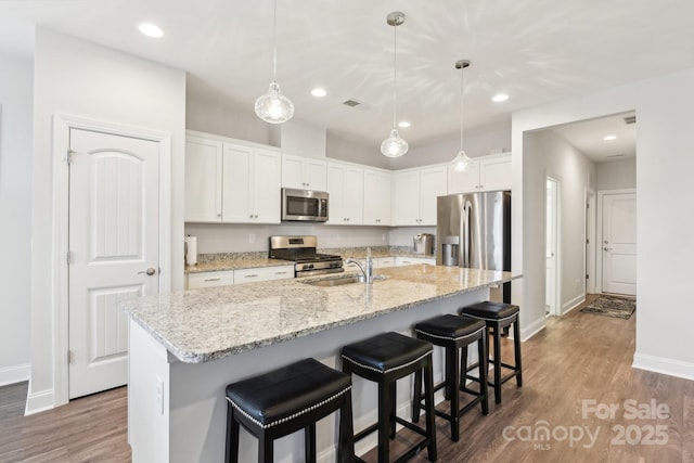 kitchen with pendant lighting, sink, white cabinets, stainless steel appliances, and a center island with sink