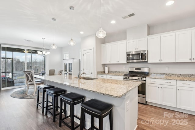 kitchen featuring white cabinetry, decorative light fixtures, a kitchen island with sink, and appliances with stainless steel finishes