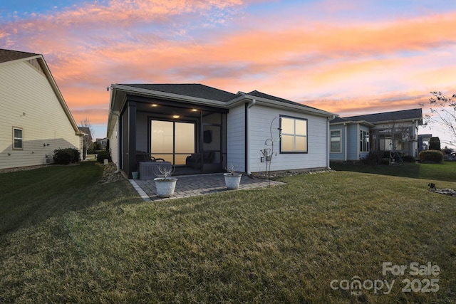 back house at dusk with a patio area and a lawn