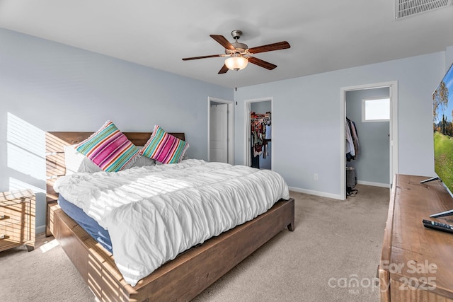 carpeted bedroom featuring a walk in closet, a closet, and ceiling fan