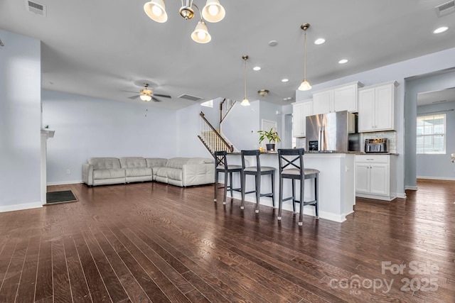 kitchen featuring pendant lighting, stainless steel fridge, dark stone countertops, white cabinets, and a kitchen bar