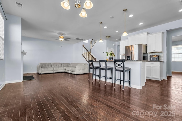 kitchen with dark wood-type flooring, a breakfast bar area, hanging light fixtures, stainless steel refrigerator with ice dispenser, and white cabinets