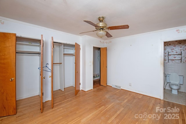 unfurnished bedroom featuring ensuite bathroom, crown molding, light hardwood / wood-style flooring, multiple closets, and ceiling fan