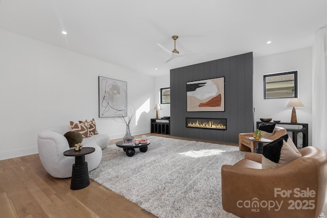 living room featuring hardwood / wood-style floors, a large fireplace, and ceiling fan