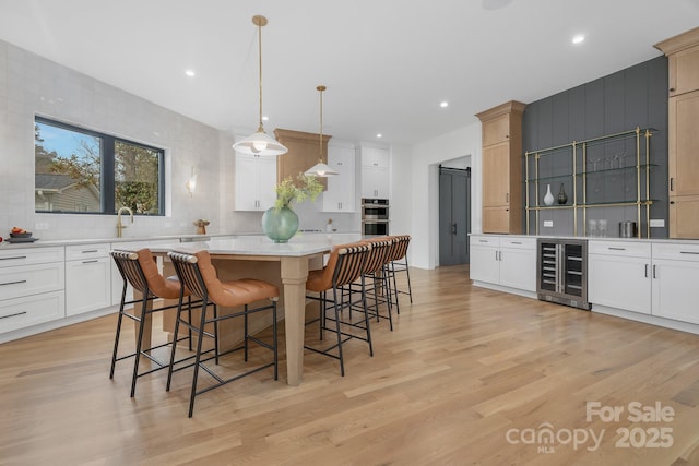 kitchen featuring wine cooler, hanging light fixtures, light wood-type flooring, a kitchen island, and stainless steel double oven