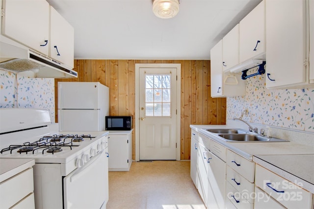 kitchen featuring sink, white cabinets, white appliances, and wood walls