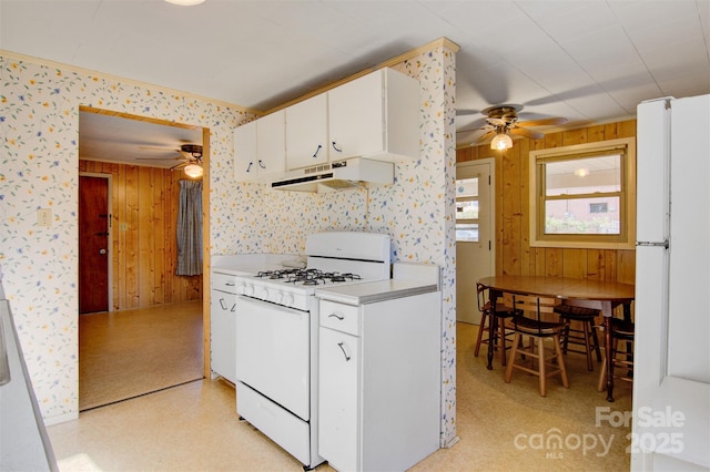 kitchen featuring white cabinetry, wooden walls, ceiling fan, and white appliances