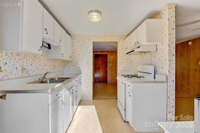 kitchen with white cabinetry, wooden walls, white range with gas cooktop, and sink