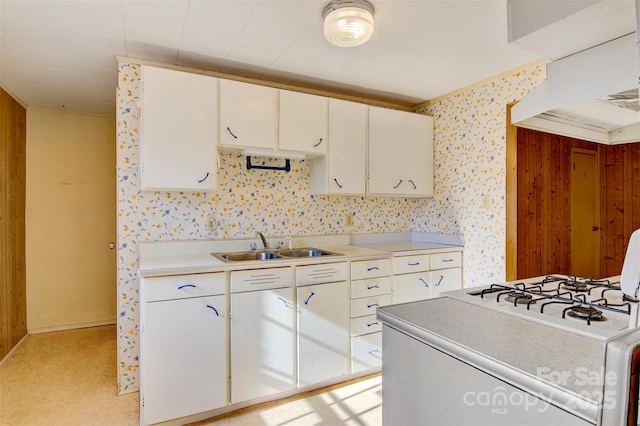 kitchen with sink, gas range gas stove, white cabinets, light colored carpet, and wood walls